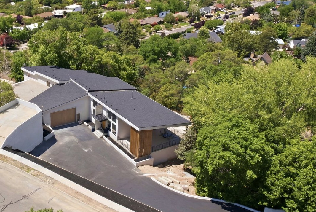 Contemporary architectural style with a dark shingle roof, extensive vertical window arrays, and a wood-finish garage door