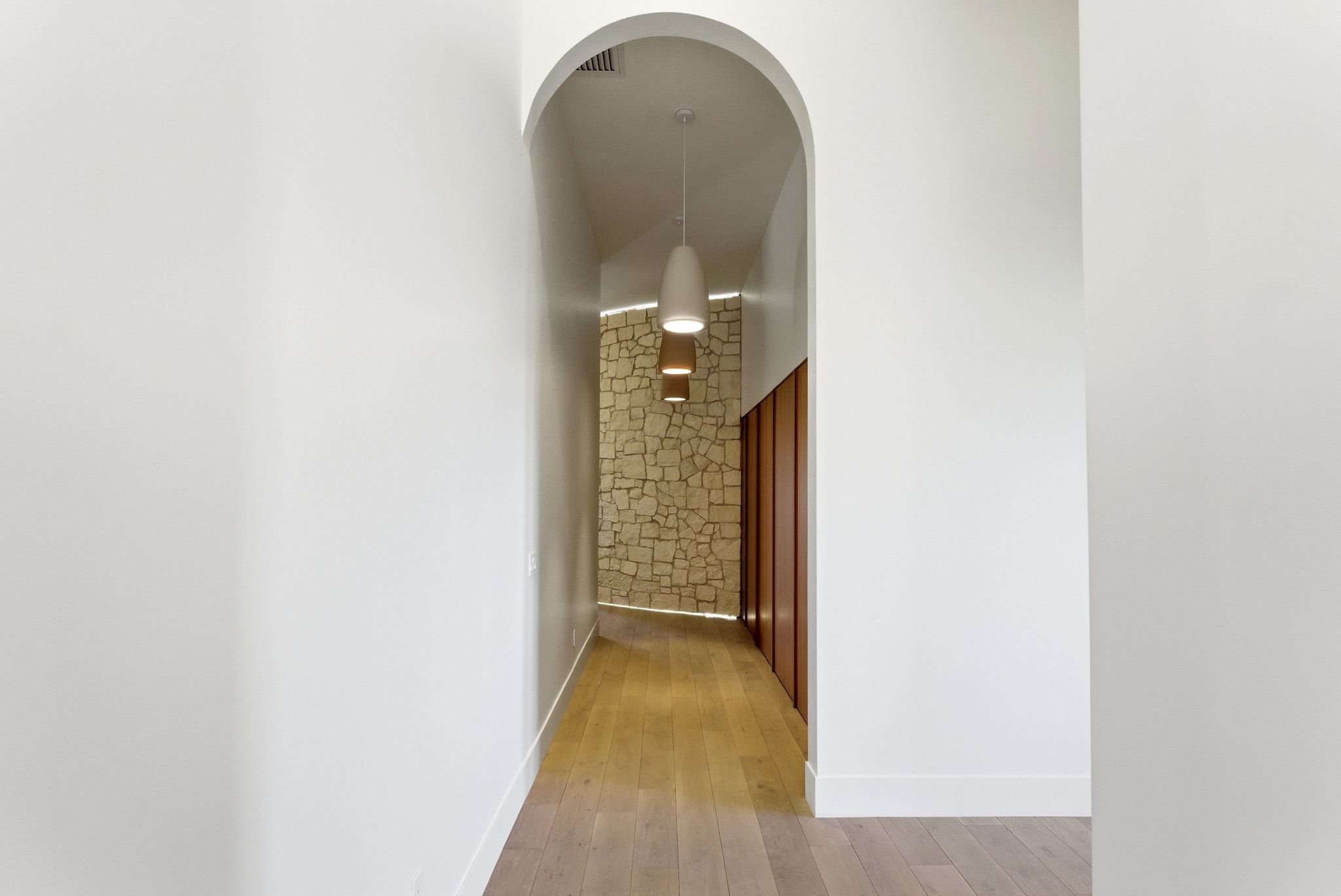 Archway entry to a hallway featuring stone wall accents, wood-finish flooring, recessed lighting, and modern pendant light fixtures