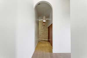 Archway entry to a hallway featuring stone wall accents, wood-finish flooring, recessed lighting, and modern pendant light fixtures