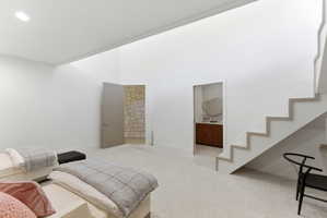 Open concept living space featuring a high ceiling, recessed lighting, carpet flooring, a floating staircase with light wood-finish treads, and a doorway leading to a room with stone walls
