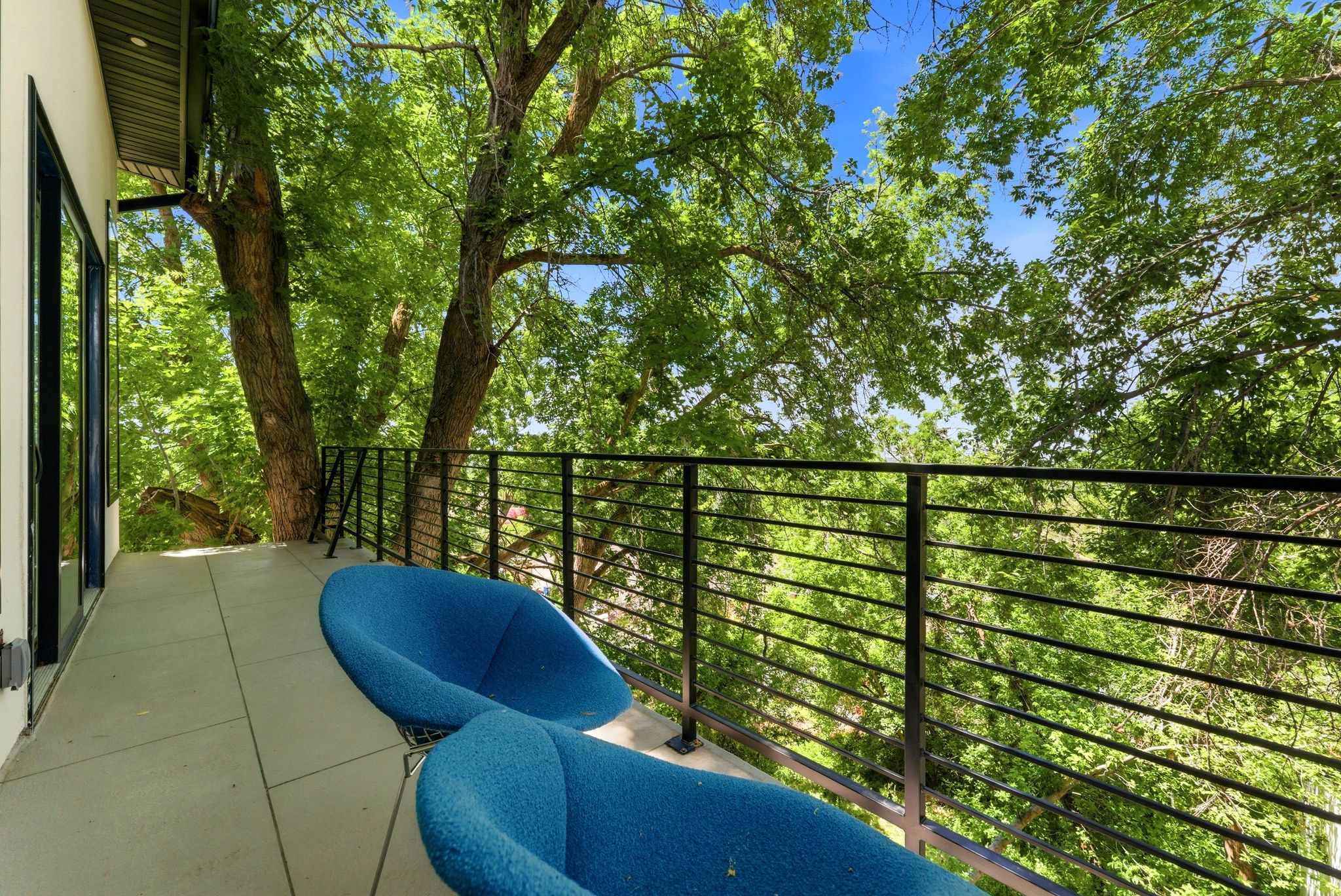Private balcony featuring a concrete surface, black metal railing, and expansive tree canopy