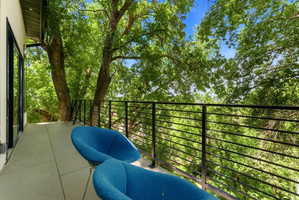 Private balcony featuring a concrete surface, black metal railing, and expansive tree canopy