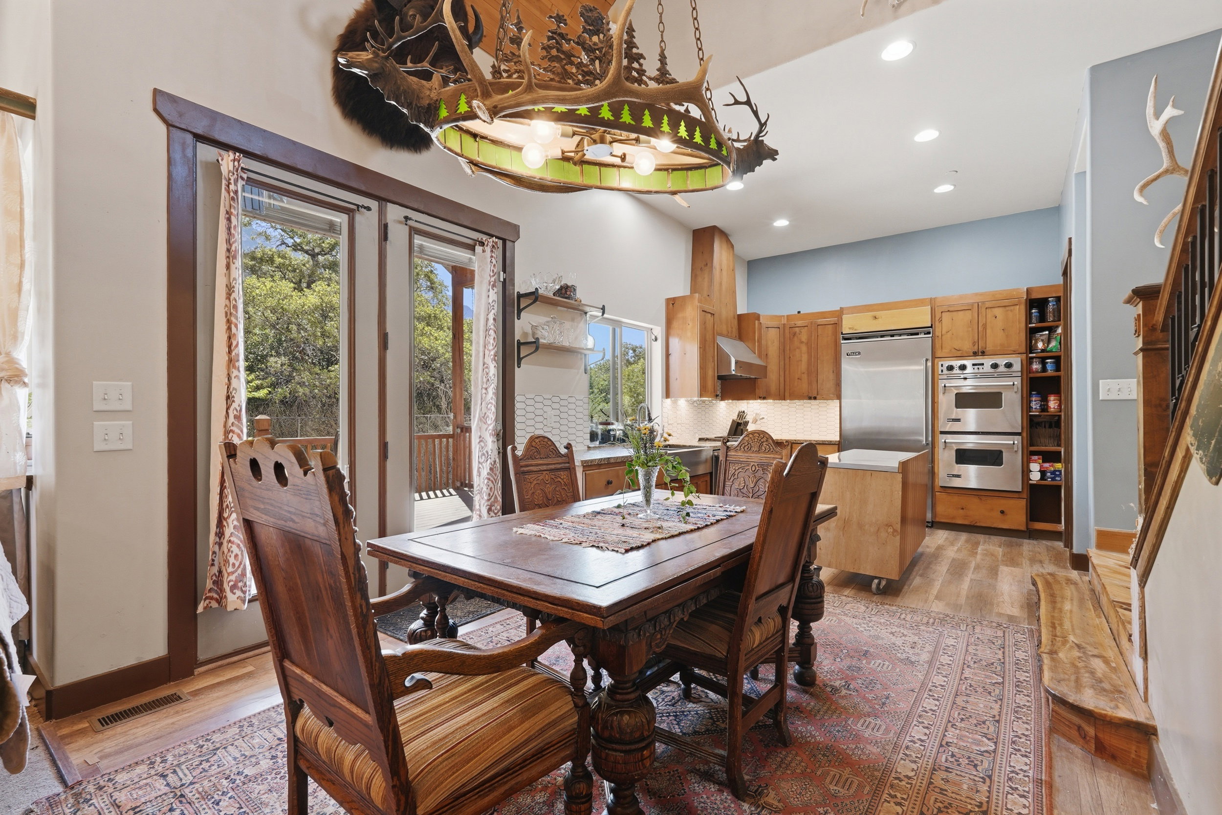 Open-concept kitchen and dining area featuring wood-finish flooring, custom wood cabinetry, stainless steel appliances, and a double oven
