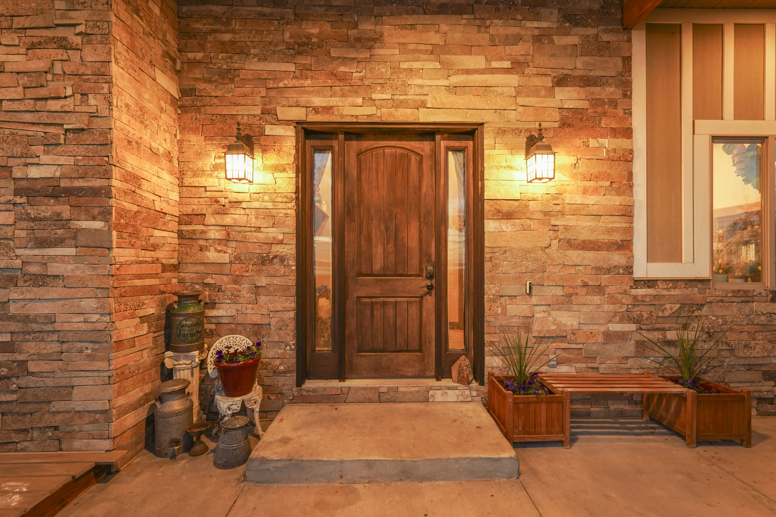 Stone veneer exterior featuring a solid wood entry door with glass sidelights, two wall-mounted lanterns, and a concrete stoop