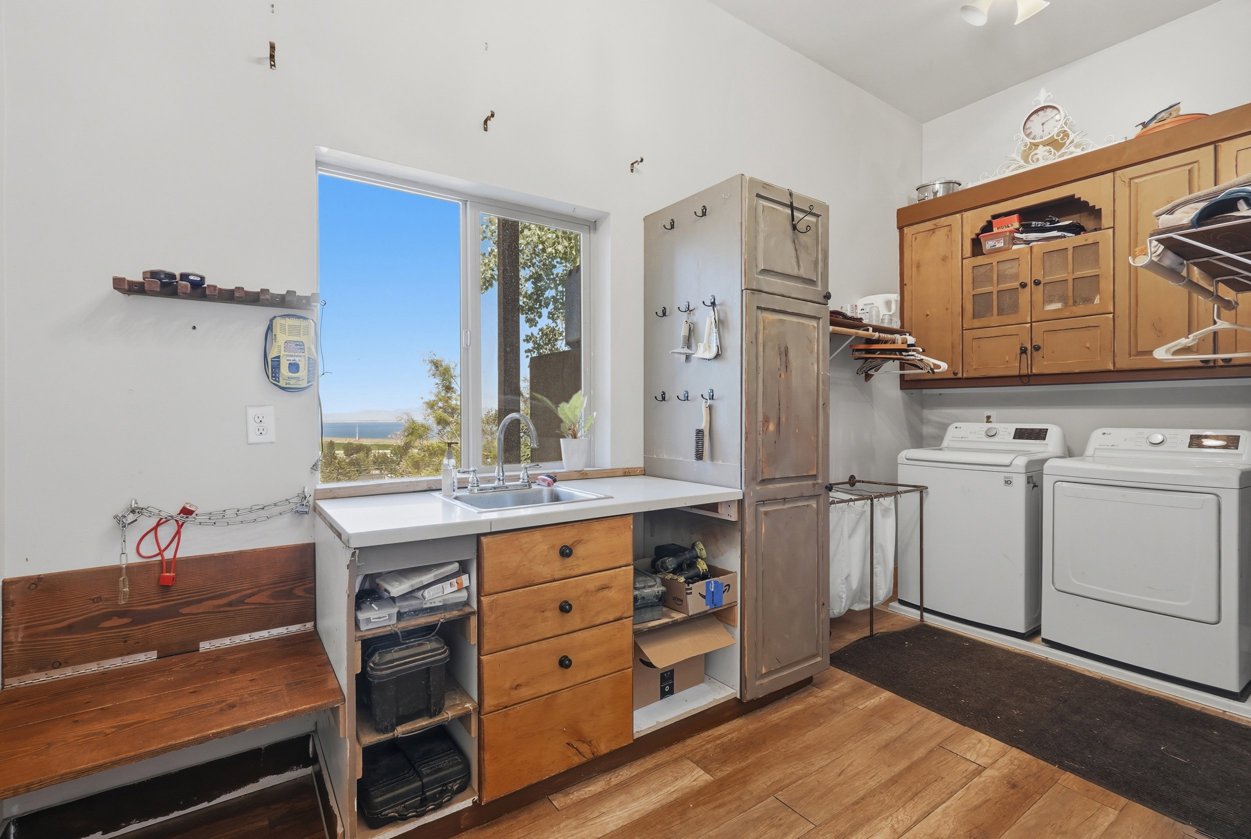 Dedicated utility space featuring wood-finish flooring, a window offering an exterior landscape, a utility sink with a countertop, built-in cabinetry, and a washer and dryer