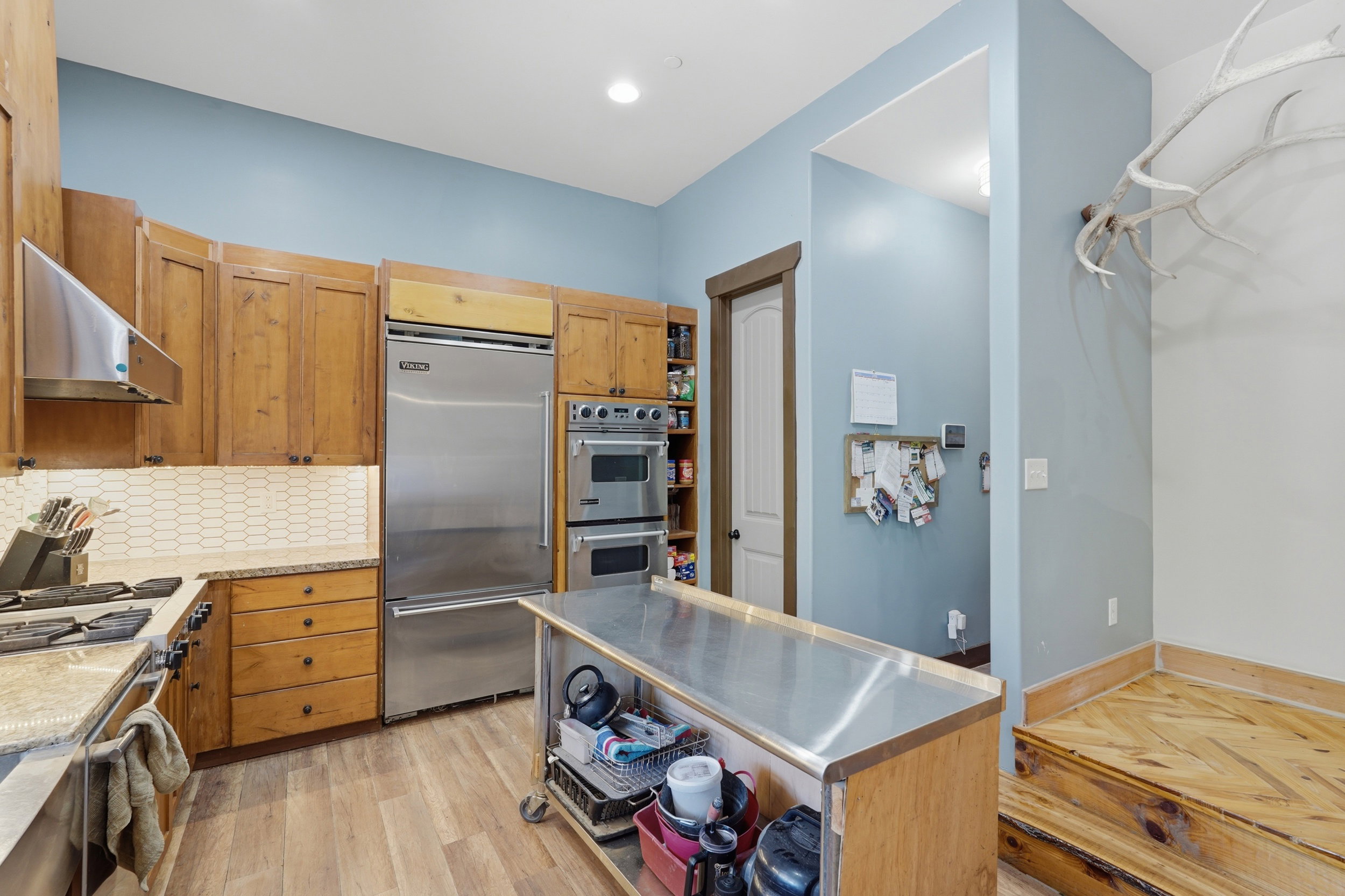 Gourmet kitchen featuring wood-finish cabinetry, stainless steel appliances, a tiled backsplash, granite countertops, and wood-finish flooring