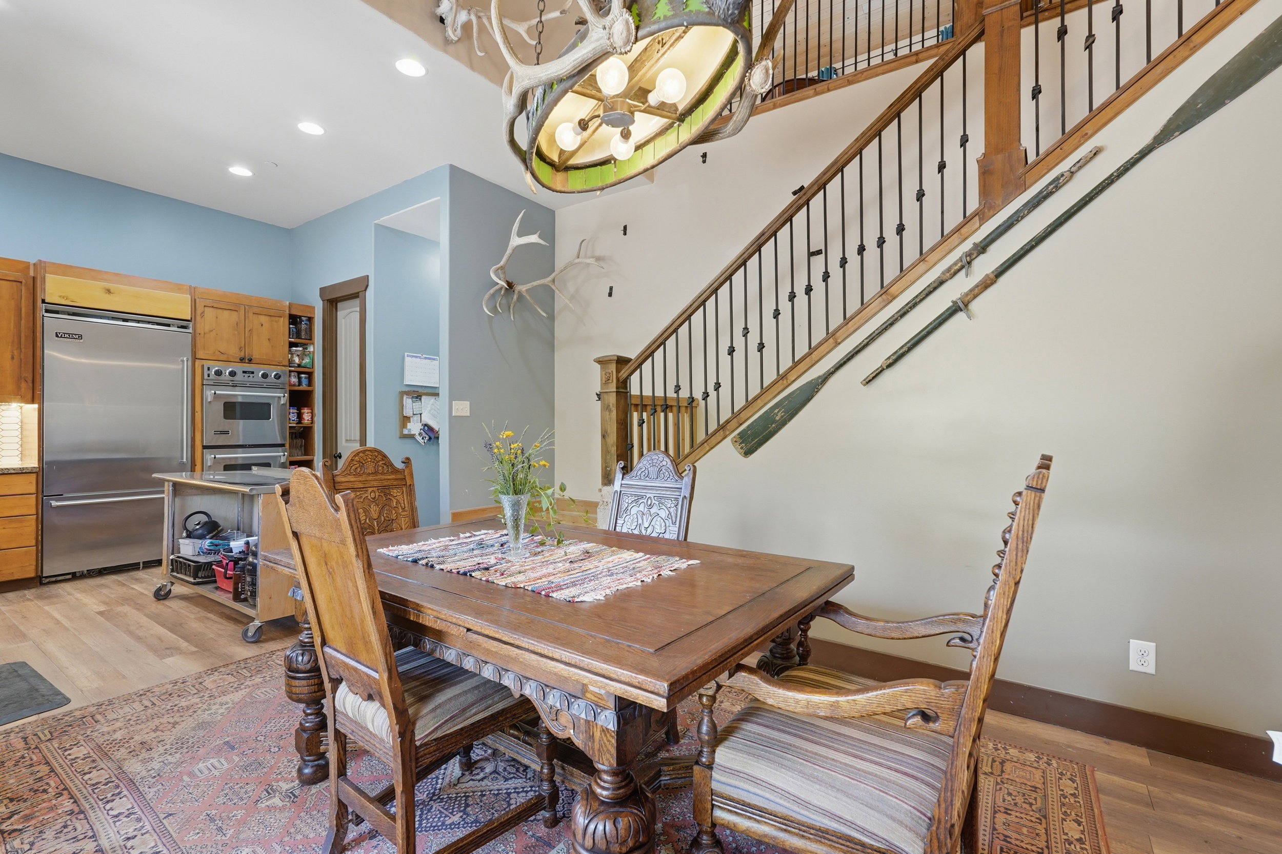 Open-concept dining area featuring a grand staircase with wrought iron balusters and a custom antler chandelier