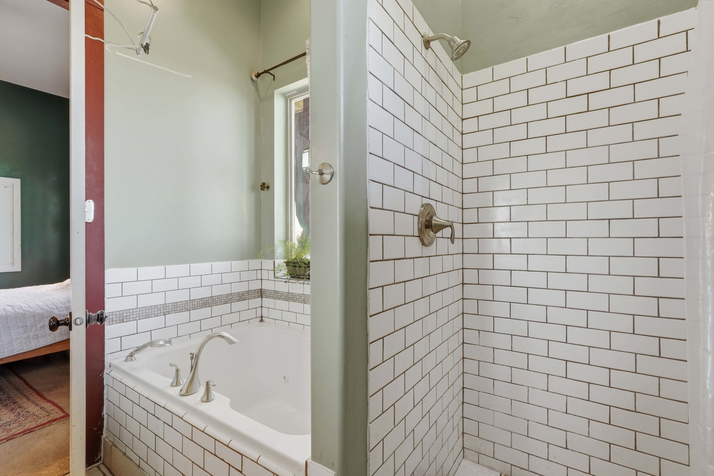 Subway tile shower and garden tub combination featuring brushed nickel fixtures, a mosaic tile accent band, and a window for natural light