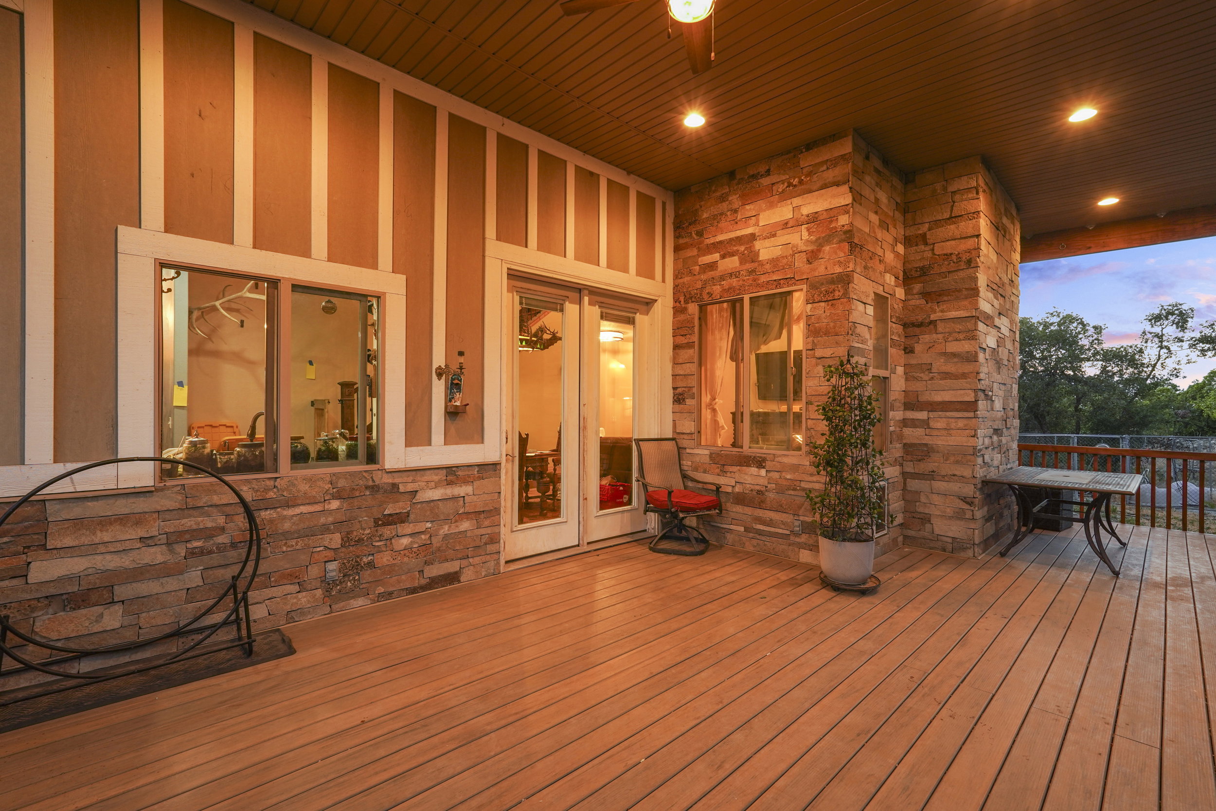 Spacious covered patio featuring wood-finish flooring, stone accent walls, recessed lighting, and a ceiling fan