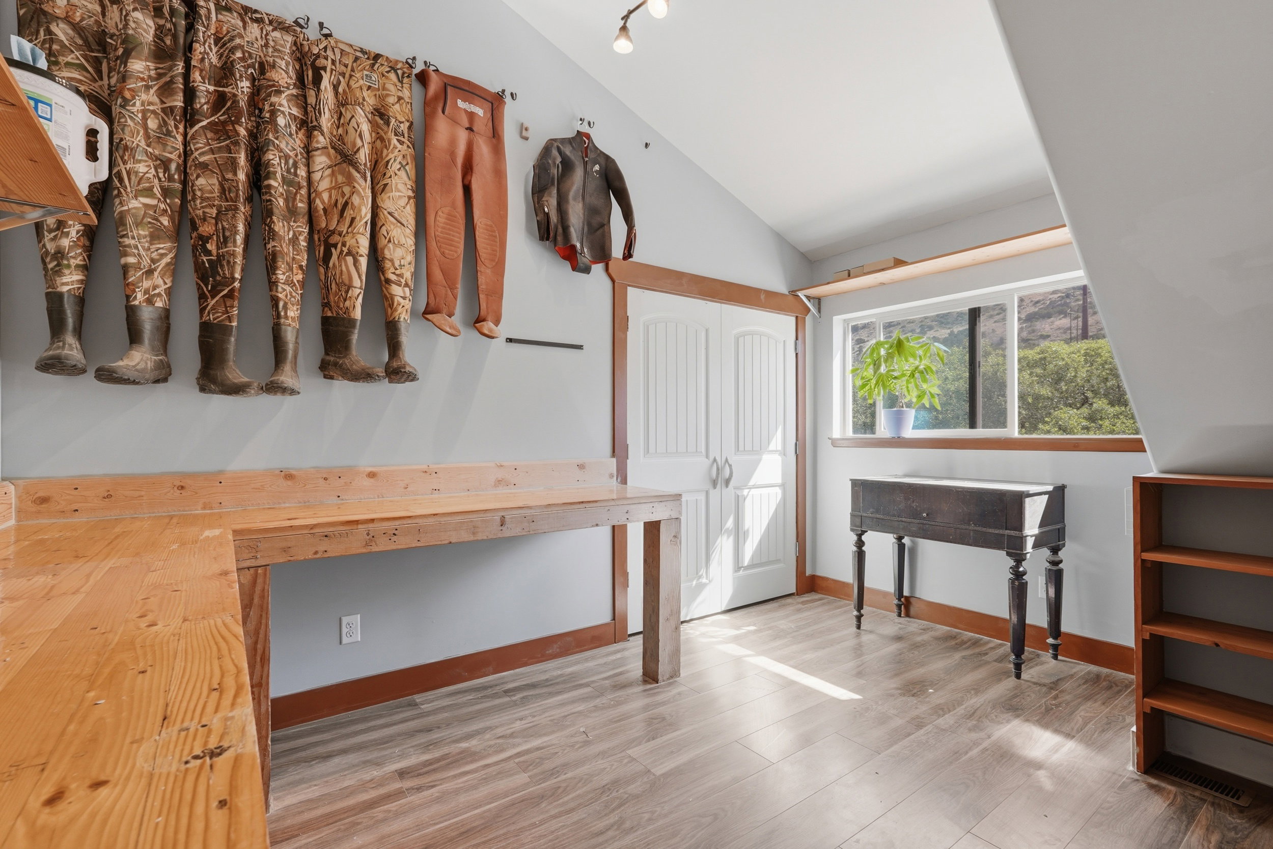 Vaulted ceiling room with wood-finish flooring, two large built-in wooden workbenches, and a double-door closet