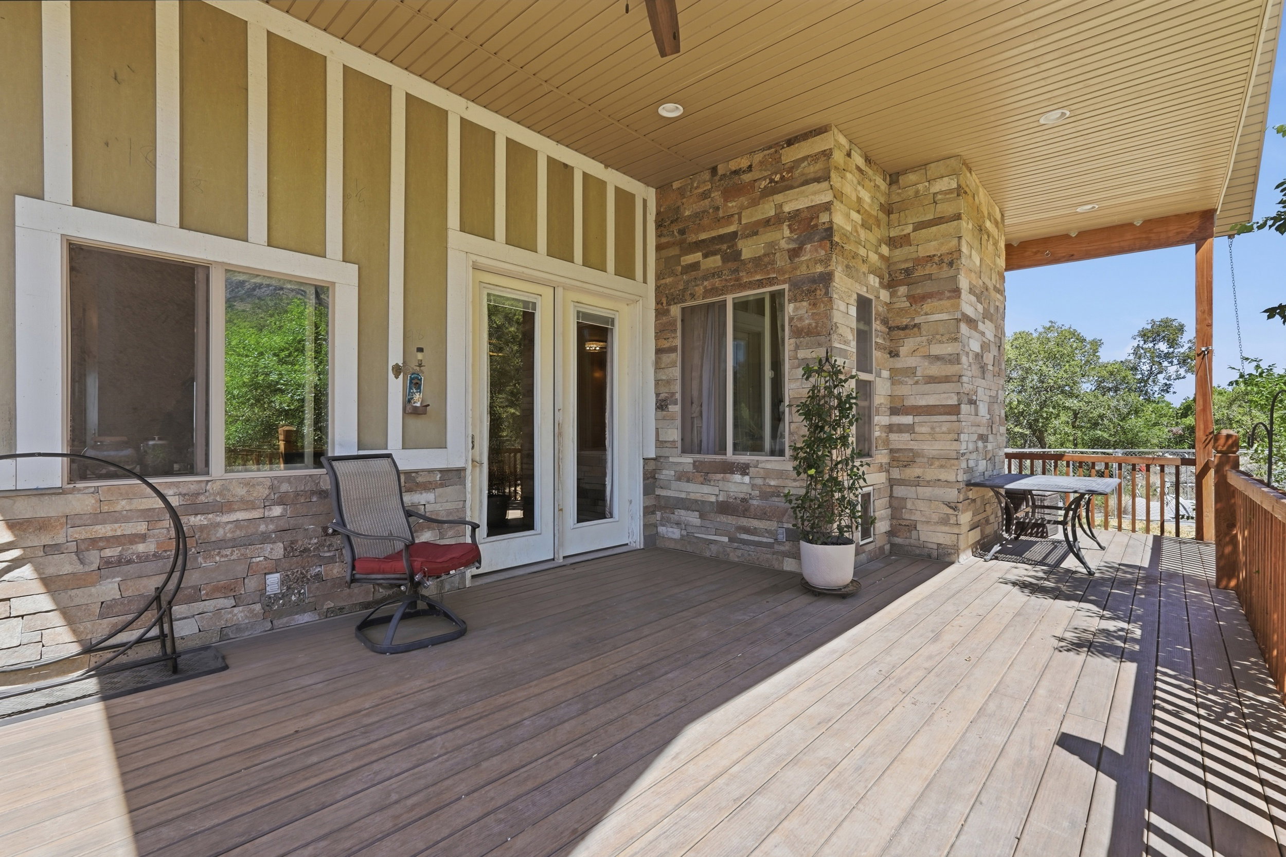 Expansive outdoor deck featuring wood-finish flooring, a stone-clad exterior wall, and white-framed double glass doors