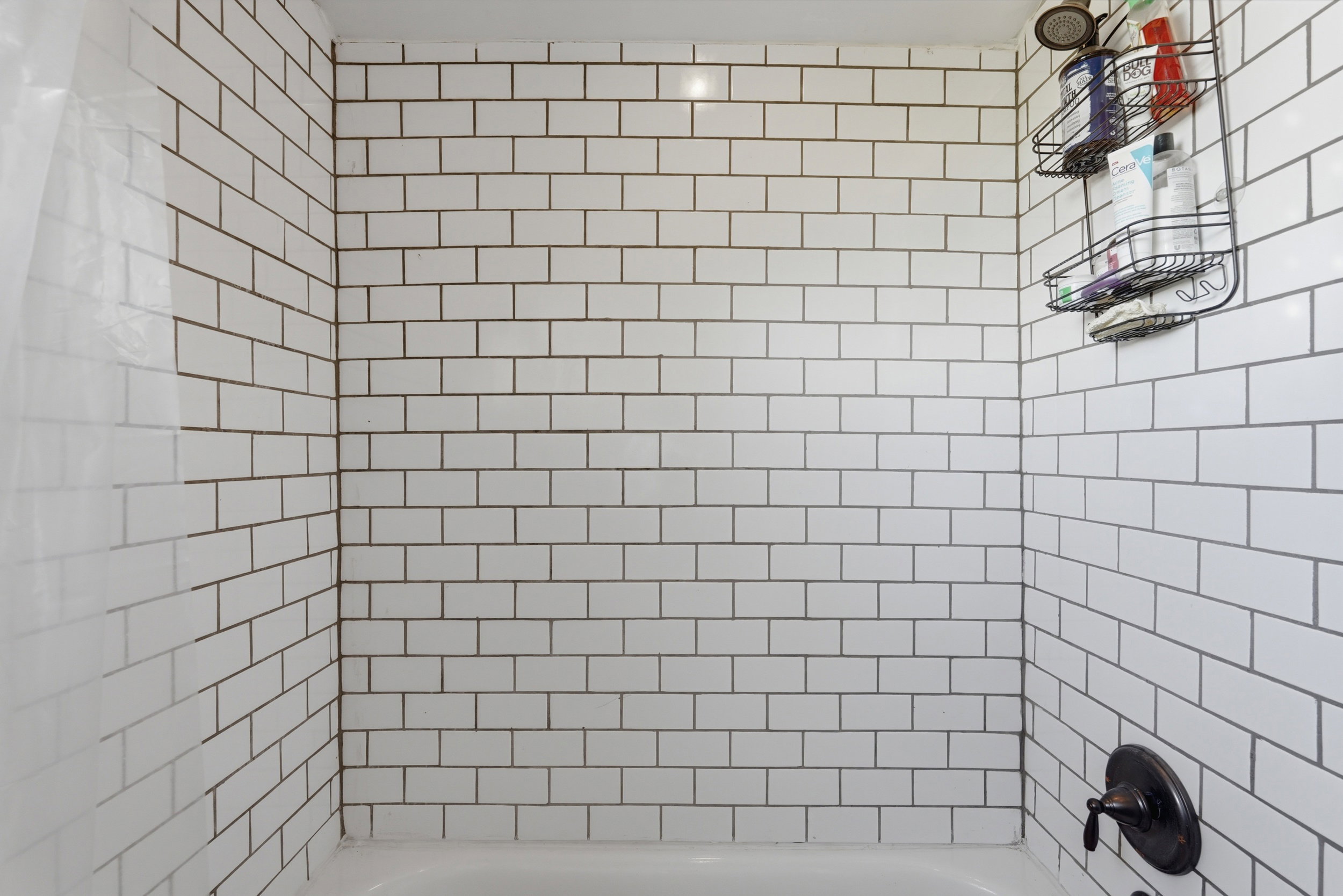 Shower enclosure featuring white subway tile surround, dark grout, a bronze-finish shower head, and matching bronze-finish faucet