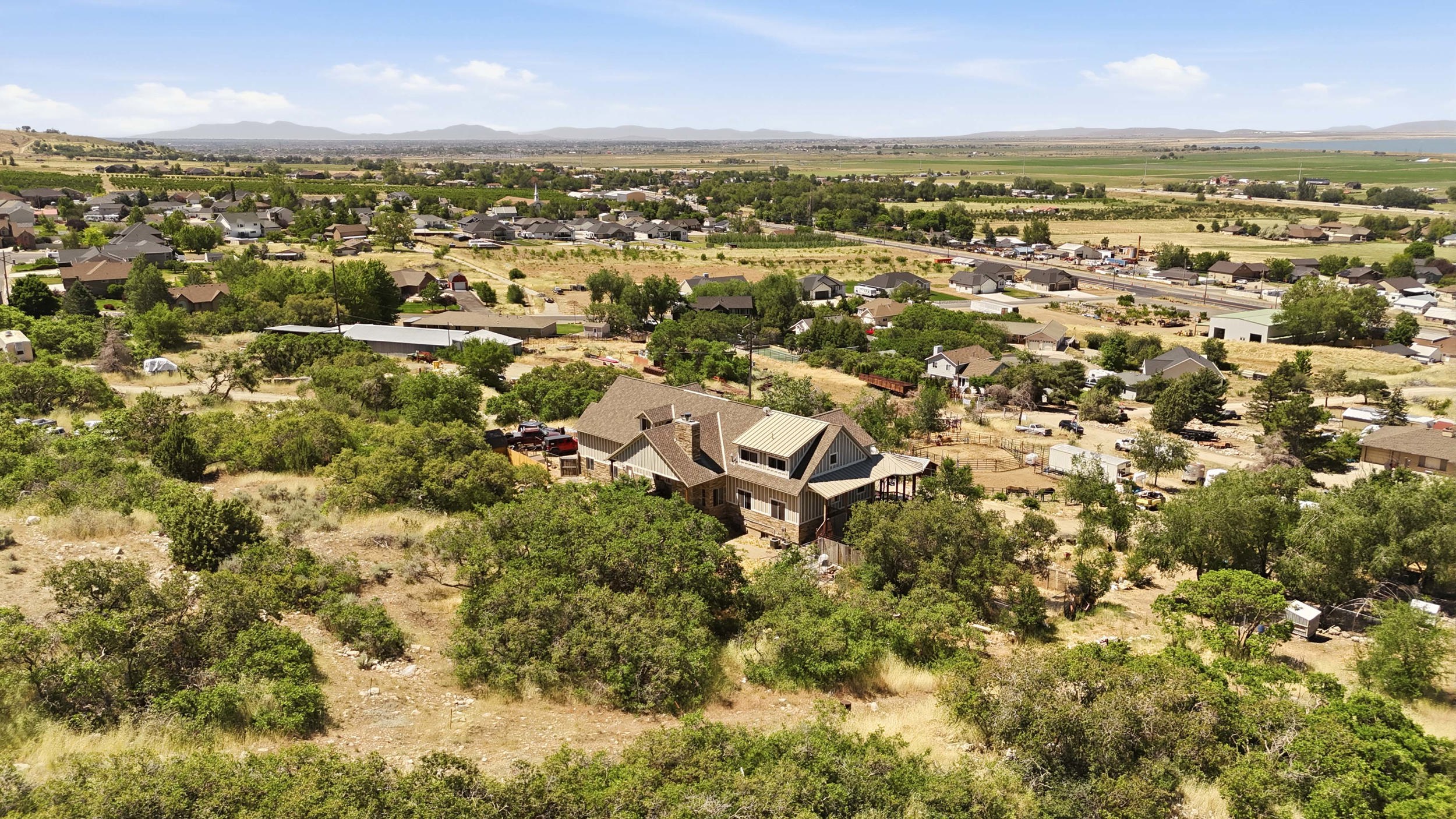 Rural landscape featuring a multi-story residence with multiple rooflines, a light-colored exterior, and surrounding natural foliage