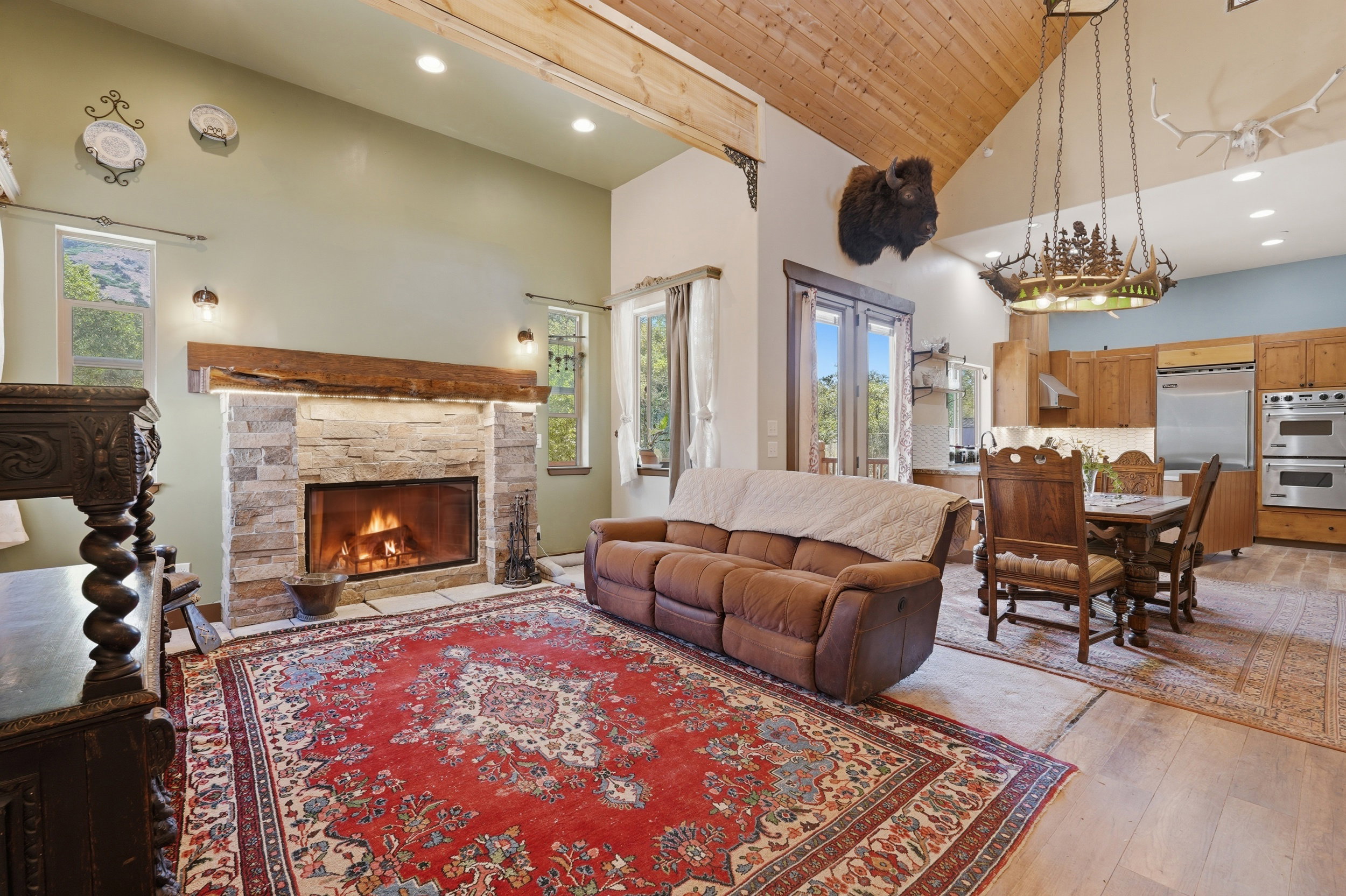 Vaulted wood-plank ceilings frame an open-concept living space featuring a stone fireplace with a substantial wood mantel