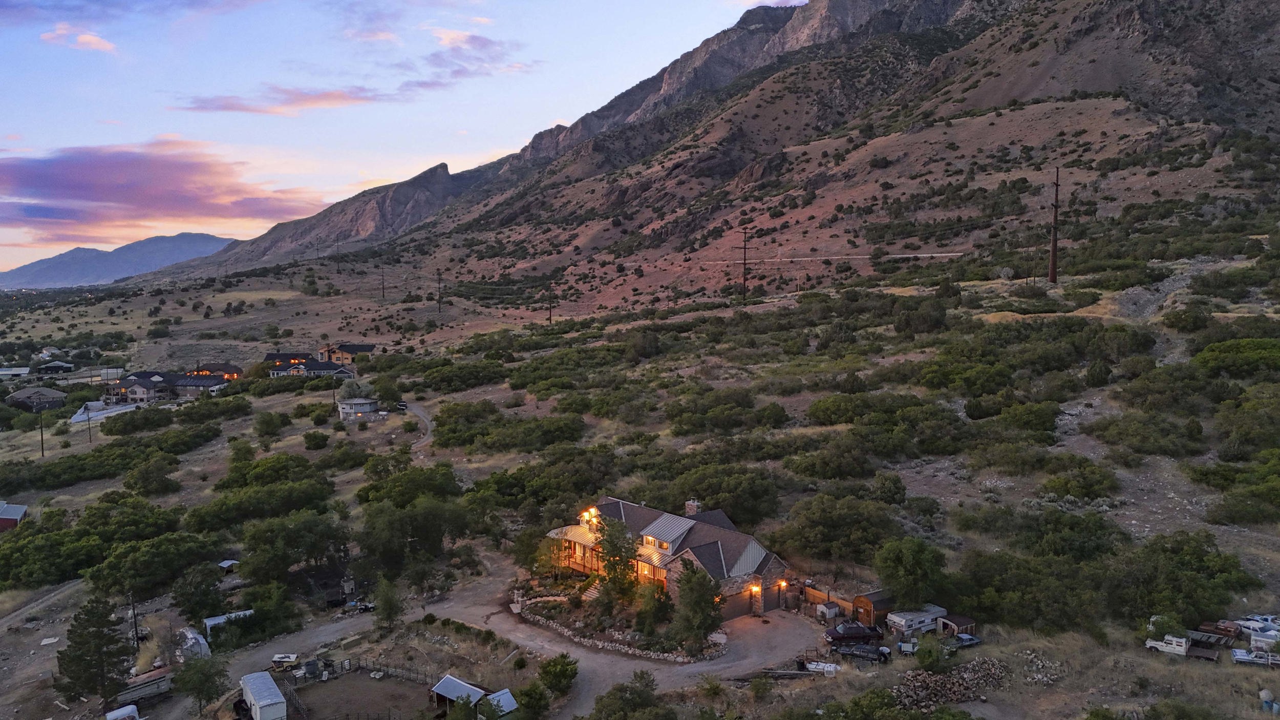 Expansive property set against a mountain backdrop, featuring a multi-level residence with stone accents and a prominent chimney