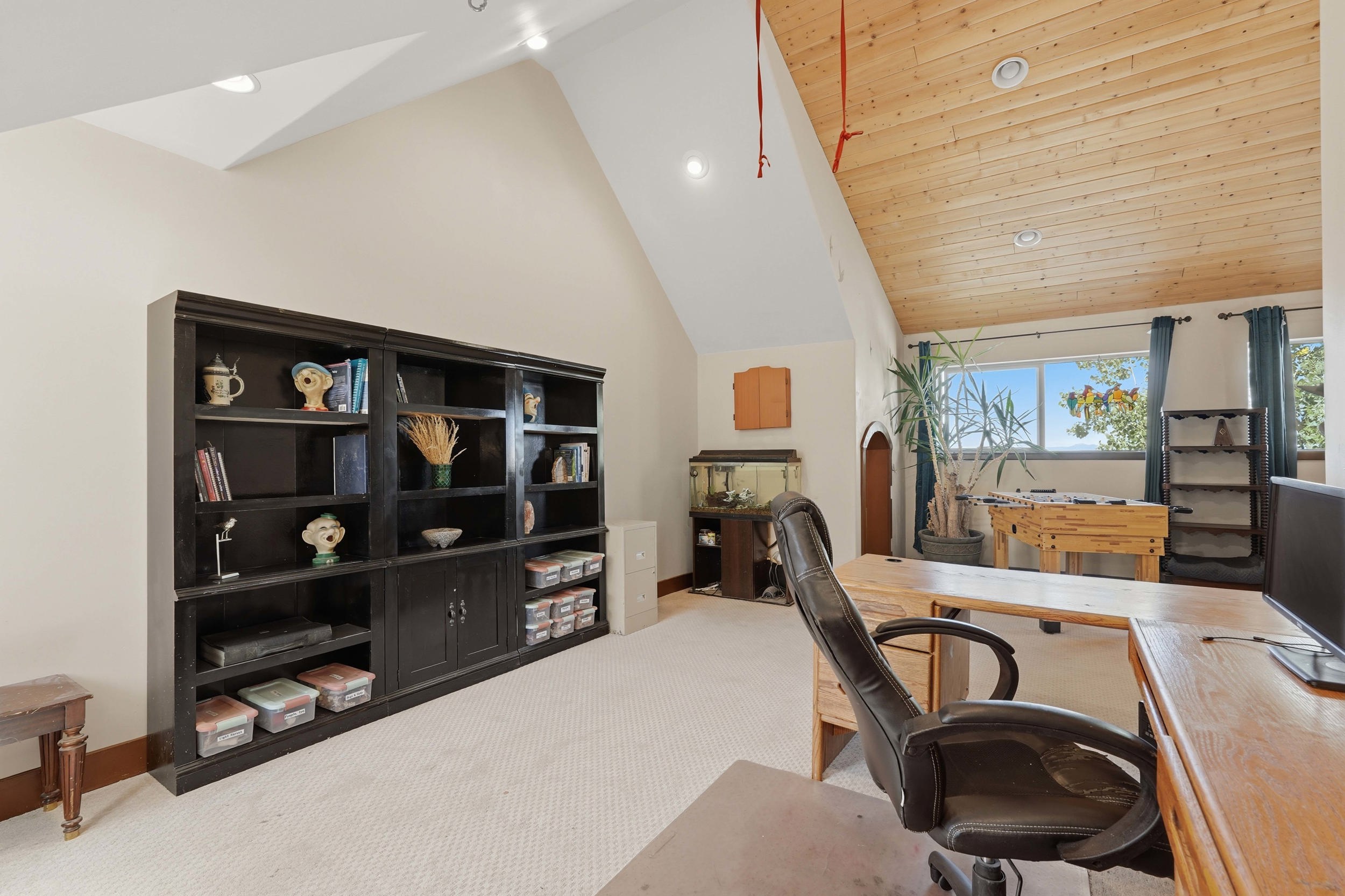 Room featuring a vaulted ceiling with wood-finish paneling, a full-wall built-in bookcase, recessed lighting, a large window, and light-toned carpet flooring