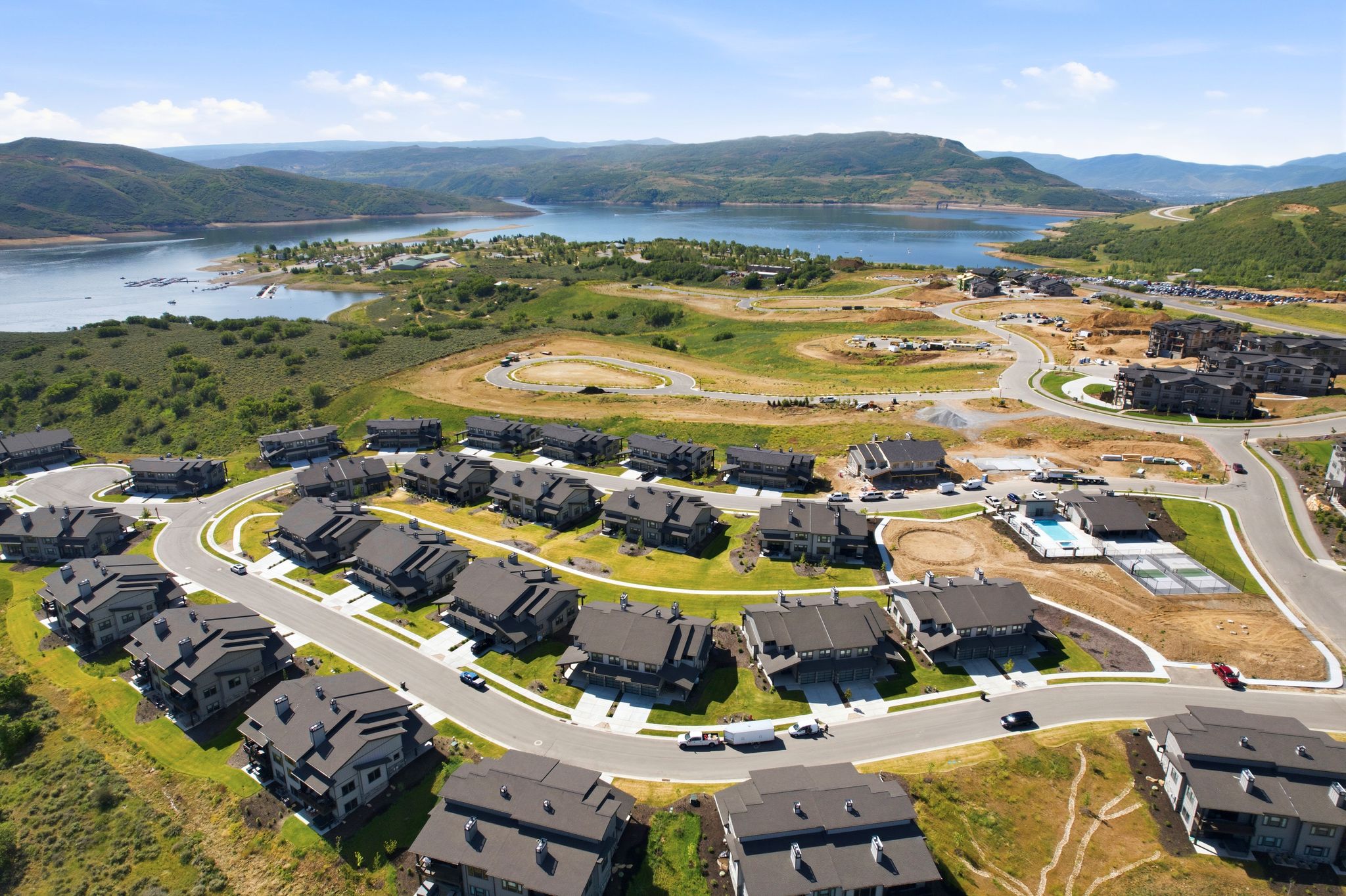 Modern residential development featuring multiple dark-roofed homes, paved roadways, and green landscaping