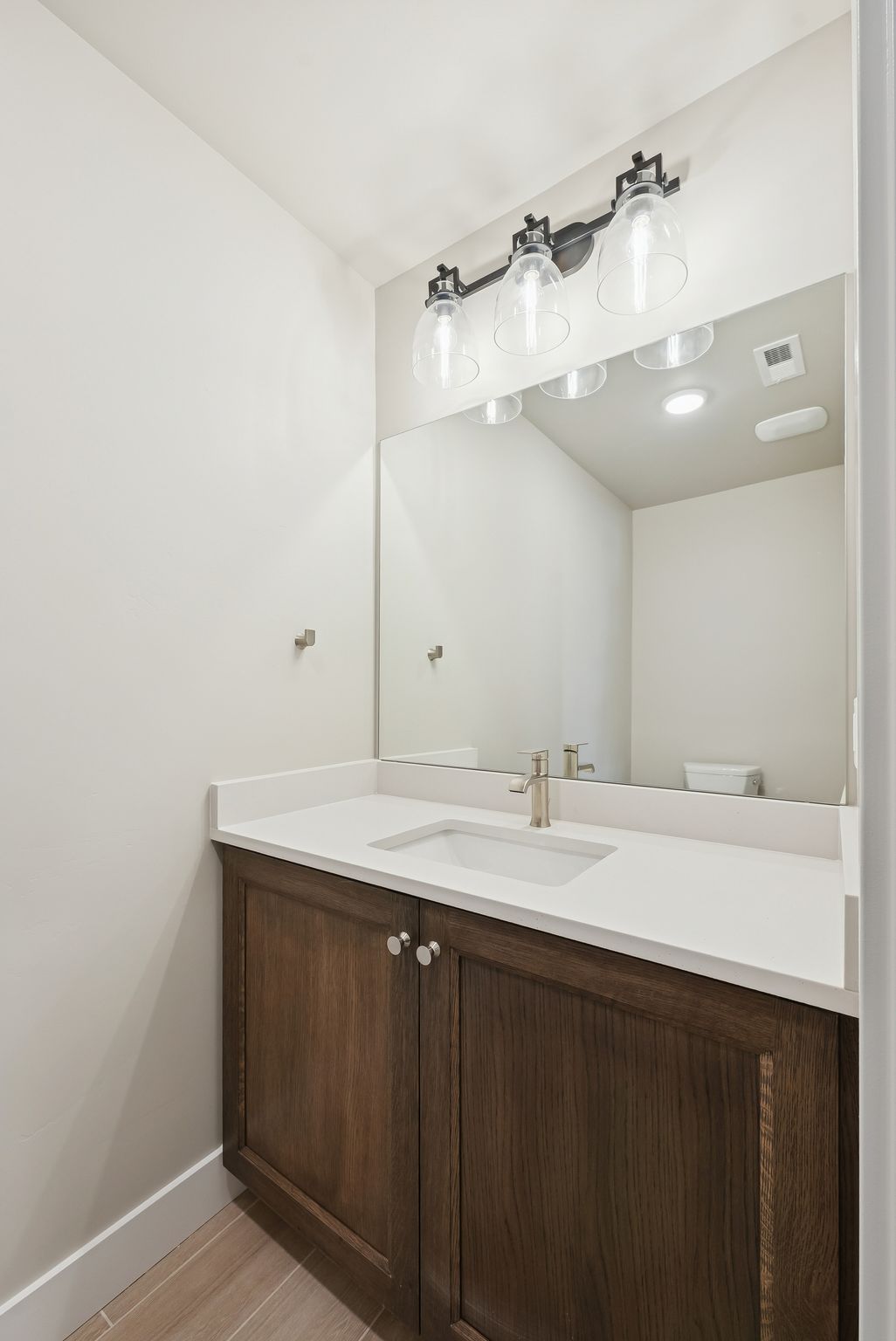 Vanity with wood-finish cabinetry, white countertop, and integrated sink
