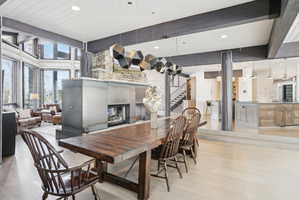 Expansive open-concept living area featuring light wood-finish flooring, a contemporary fireplace with a stone and metal surround, and a vaulted ceiling with exposed beams