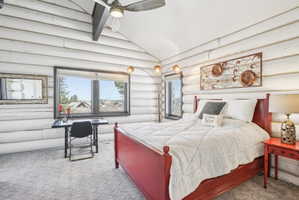 Bedroom featuring distinctive log walls, a vaulted ceiling with a ceiling fan, and a large window offering exterior scenery