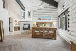 Spacious bedroom featuring log-style wall finishes, a stone-clad fireplace with a built-in firebox, and high vaulted ceilings with exposed beams