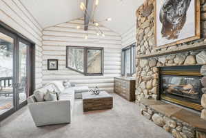 Vaulted ceiling with exposed wood beams, a stone-clad fireplace with a hearth, full-light French doors, and rustic wood-finish walls