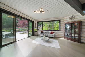 Spacious interior featuring a large sliding glass door, a picture window, wood-finish flooring, log-style walls, and a planked ceiling with a contemporary light fixture