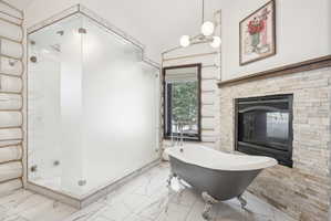 Freestanding clawfoot tub and a stone-clad fireplace with a dark wood mantel