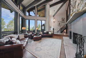 Great room featuring expansive windows, wood-finish flooring, exposed ceiling beams, a stone fireplace with a metal surround, and a prominent log column