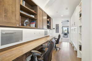Dedicated workspace featuring a long wood-finish countertop, built-in upper cabinetry with open shelving, integrated under-cabinet lighting, and white built-in storage with open shelving