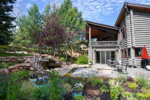 Log-sided residence with stone hardscaping, a multi-level patio, built-in fire pit, and upper-level covered balcony