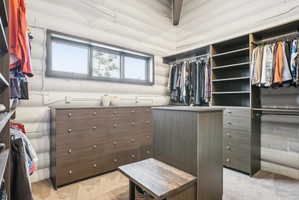 Spacious walk-in closet featuring extensive custom wood-finish cabinetry, built-in shelving, multiple hanging rods, and a window providing natural light