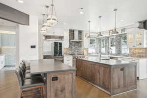 Gourmet kitchen featuring a large central island with integrated sink, wood-finish flooring, white cabinetry, professional-grade stainless steel appliances, and a stacked brick backsplash