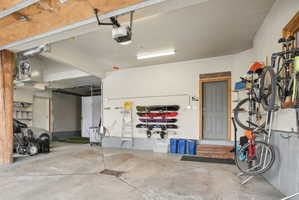 Spacious garage featuring a concrete floor, exposed wood ceiling beams, overhead lighting, an overhead garage door opener, and a gray panel door
