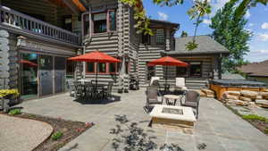 Expansive stone paver patio featuring a built-in fire pit, a hot tub with stone surround, and multiple access points to the log-style home