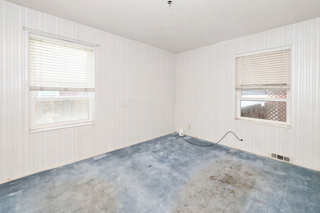 Room featuring two windows with horizontal blinds, light-colored vertical paneled walls, and blue carpeted flooring