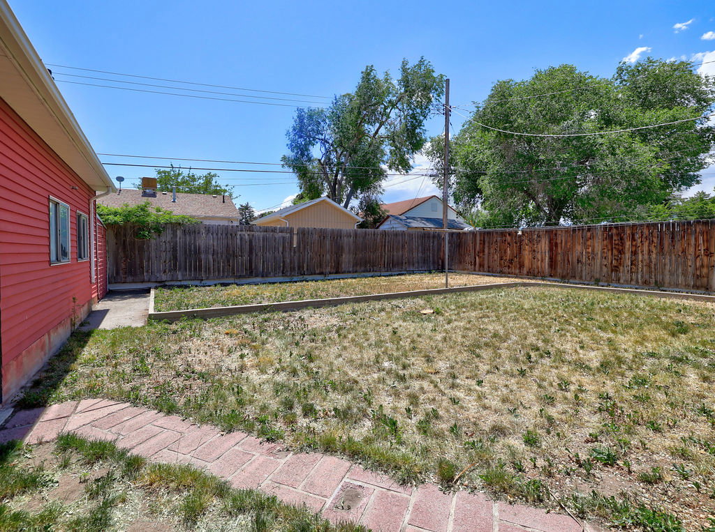 Expansive backyard featuring a red wood-sided exterior, a brick pathway, a wood privacy fence, and mature trees