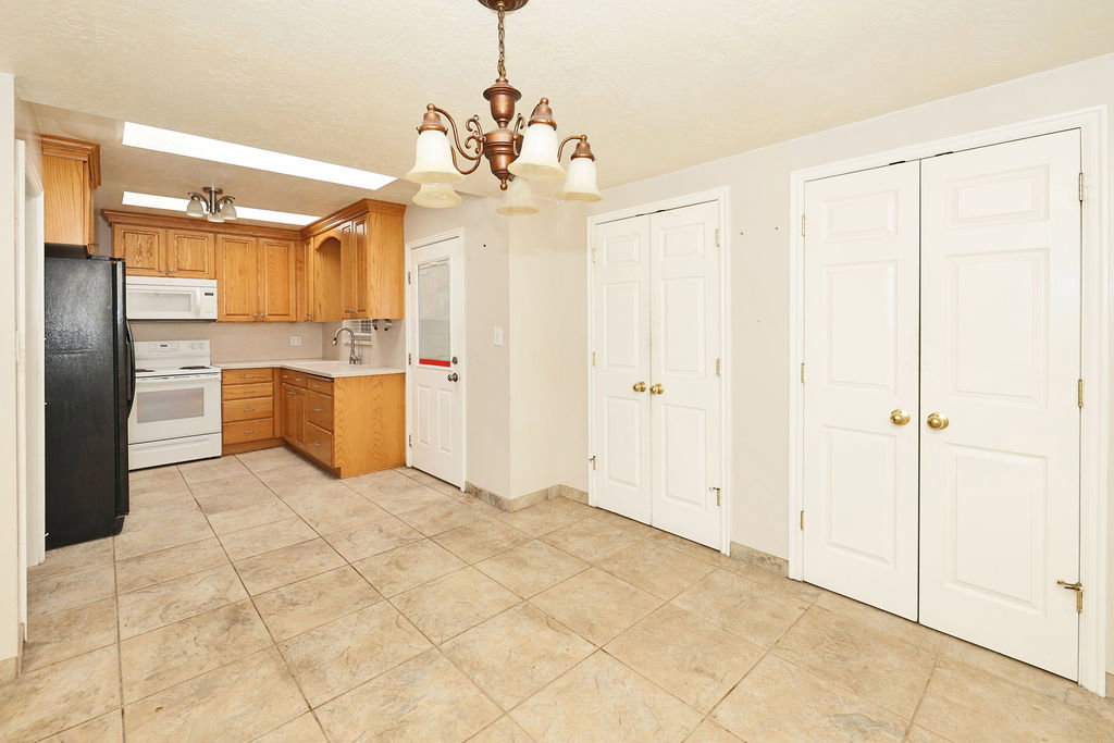 Kitchen and dining area featuring light-toned wood cabinetry, a built-in microwave, white electric range, black refrigerator, and tile flooring