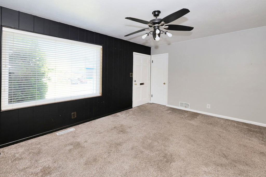 Carpeted interior space featuring a large window with horizontal blinds, a ceiling fan with integrated lighting, and a white paneled door