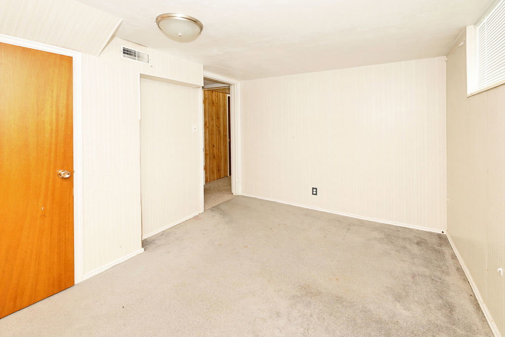 Carpeted room featuring a ceiling-mounted light fixture, a window with horizontal blinds, and a wood-finish door with a brass-tone knob