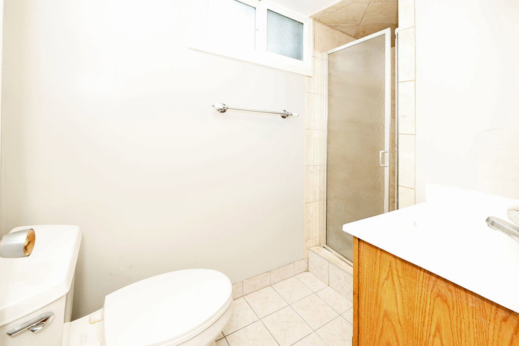 Bathroom featuring a glass-enclosed shower, wood-finish vanity with countertop, white toilet, and tiled flooring