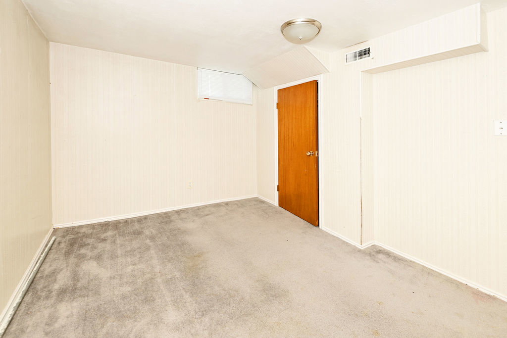 Carpeted room featuring a ceiling-mounted light fixture, a light wood-finish door, and a small, high-set window