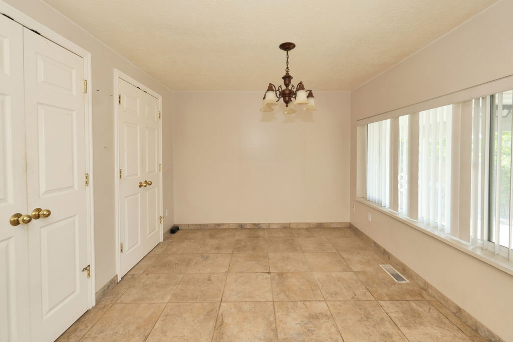 Spacious room featuring tile flooring, a multi-panel window with vertical blinds, and a traditional chandelier