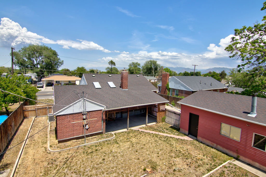 Rear exterior showcasing a covered patio, brick and siding facade, multiple skylights, and a red outbuilding