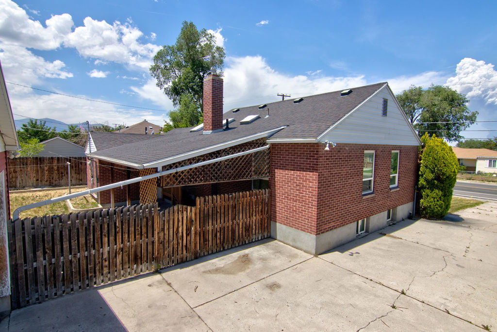 Brick exterior featuring a gabled roofline with skylights, an attached covered patio with lattice detailing, and a wood privacy fence