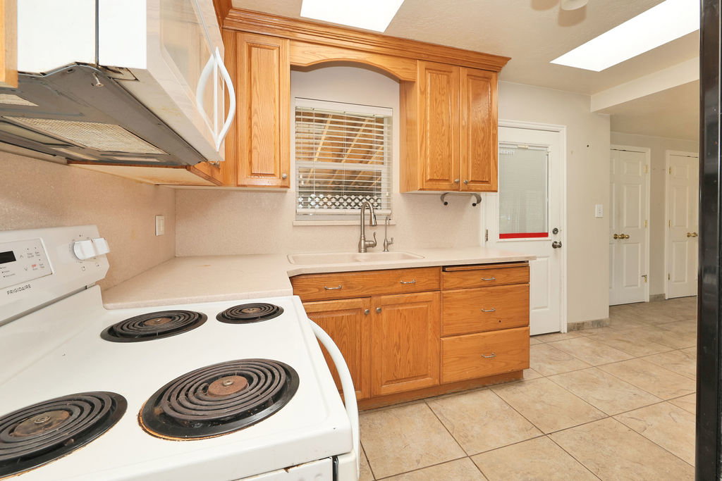 Kitchen featuring wood cabinetry, white countertops, a built-in sink with a gooseneck faucet, an electric range, and tile flooring