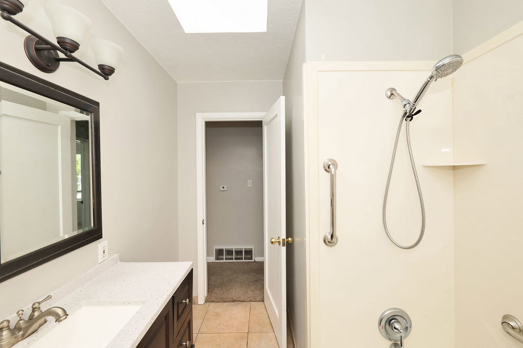 Bathroom featuring a vanity with a white speckled countertop, dark wood-finish cabinetry, a rectangular undermount sink, and a brushed nickel faucet