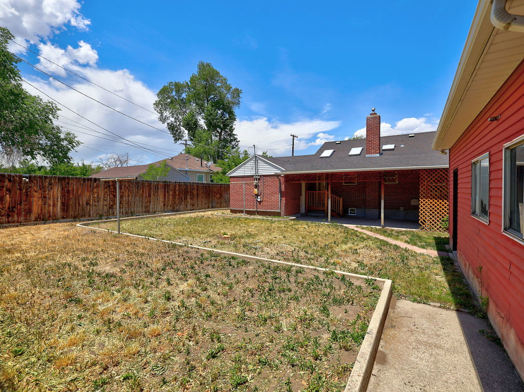 Expansive backyard featuring a wood fence, concrete pathway, and raised garden beds