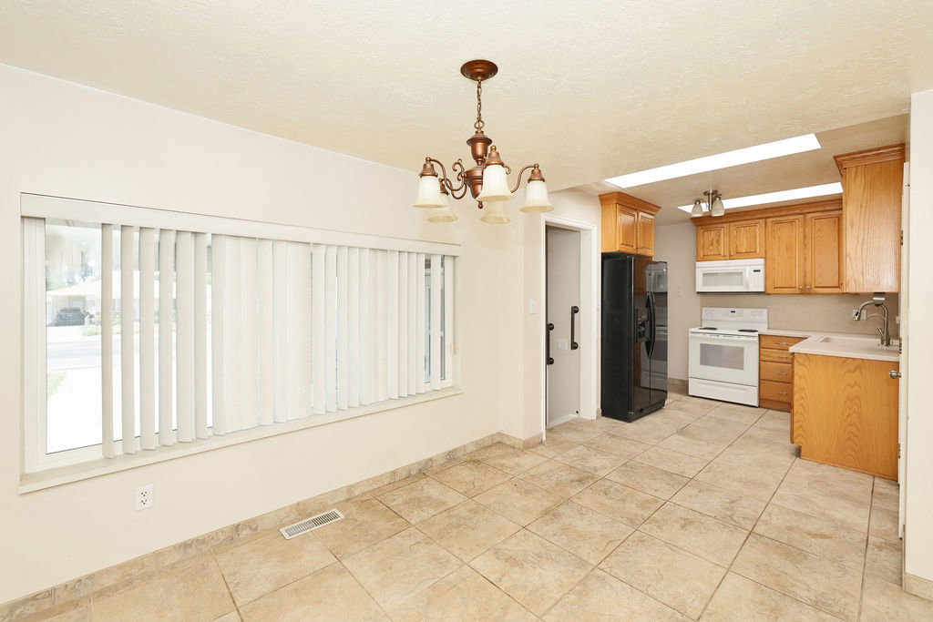 Kitchen and dining area featuring tile flooring, a window with vertical blinds, a bronze chandelier, wood cabinetry, and white appliances
