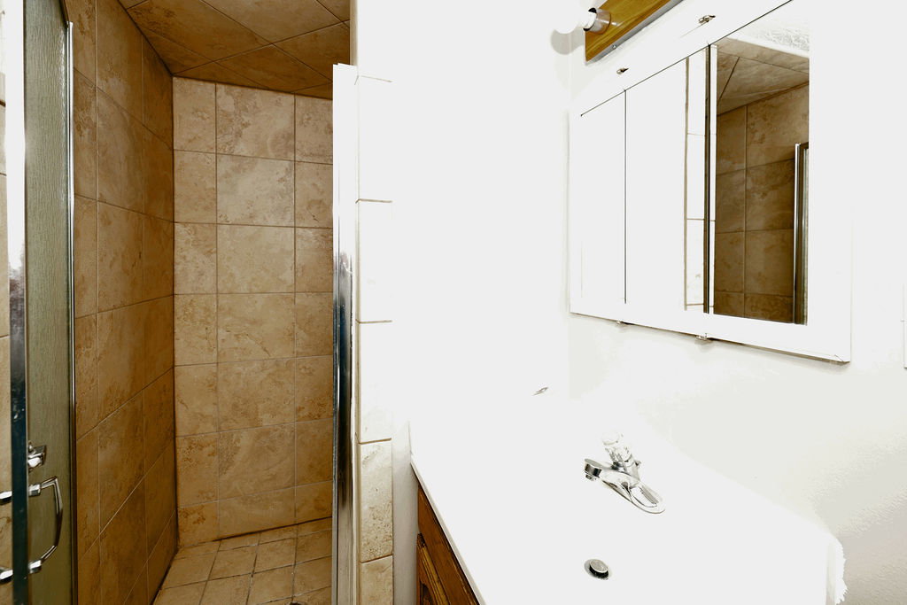 Tiled shower enclosure with a clear glass door, complemented by a white vanity with an integrated sink and a mirrored medicine cabinet